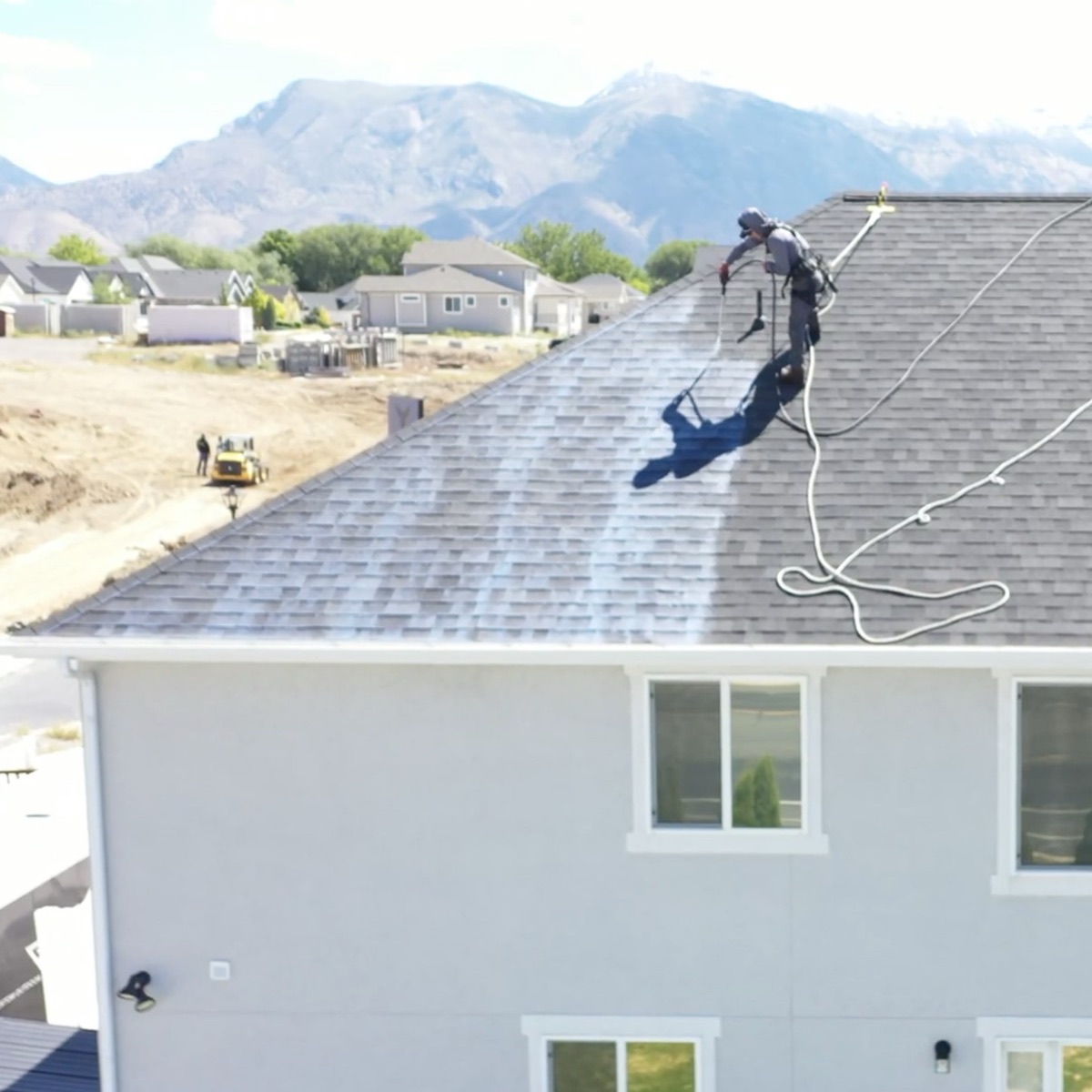 Applicator in a harness spraying HRX across an asphalt shingle roof, mountains behind